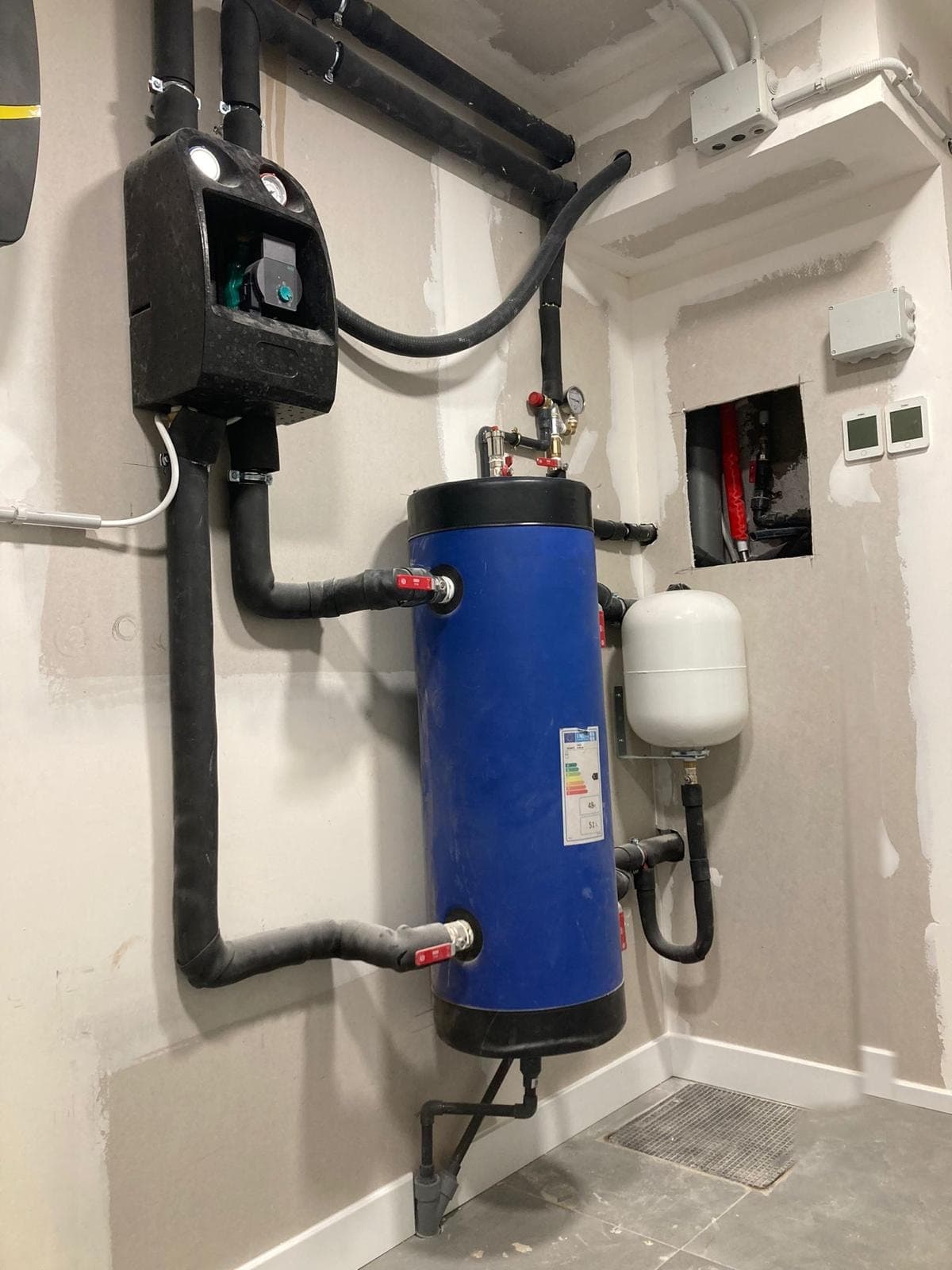 Depósito de inercia y grupo de bombeo de la instalación, con el hueco del colector abierto en la pared